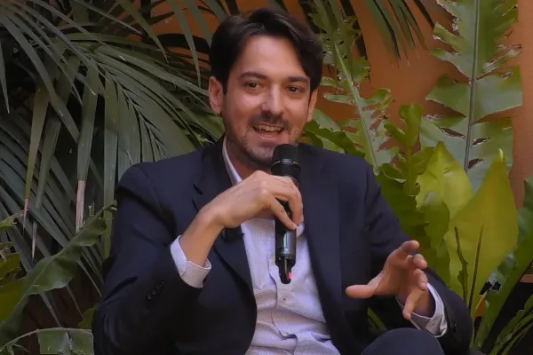 Foto a mezzo busto di Marco Battaglia, CEO di Sfridoo, con abiti eleganti e un microfono in mano, intento a parlare durante l'evento Sustainability Garden